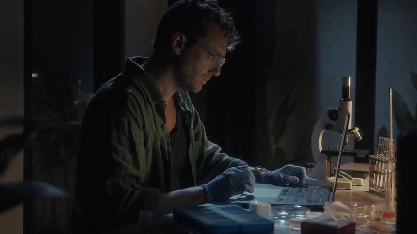 A scientist is using his laptop at his desk in the lab