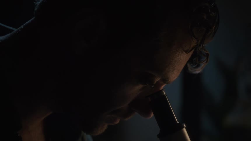 A scientist removes his glasses to look through a microscope