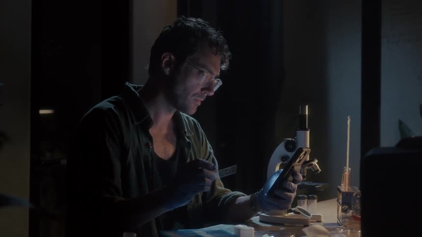 A scientist is examining a microscope slide and comparing it to his phone