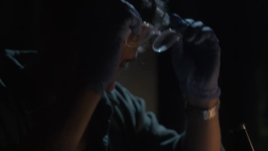 A scientist puts on glasses and studies something under a microscope in a lab