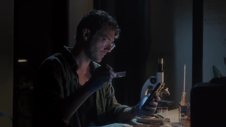 A scientist is looking at a microscope slide and using his cell phone