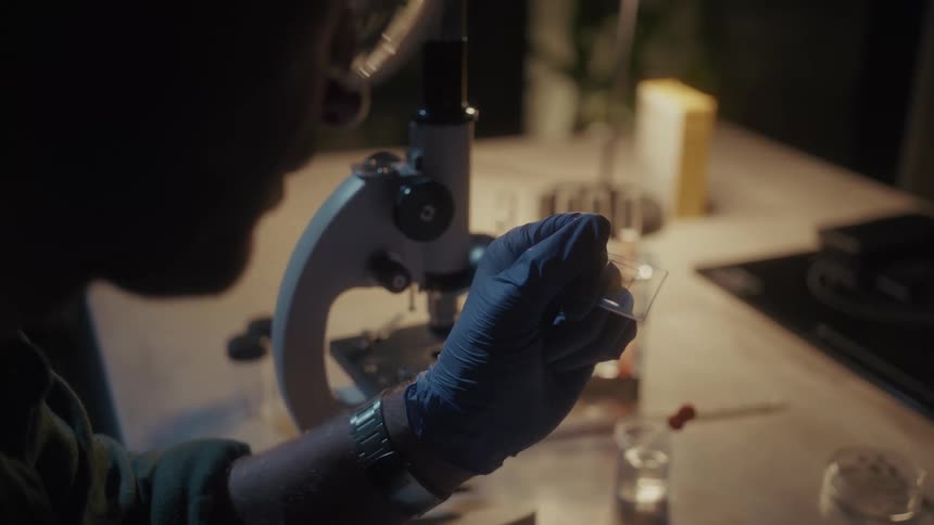 A man holds up a microscope slide to examine