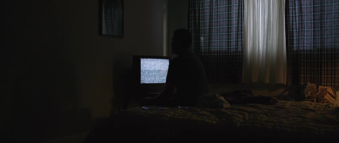 A man is sitting in front of a static filled television