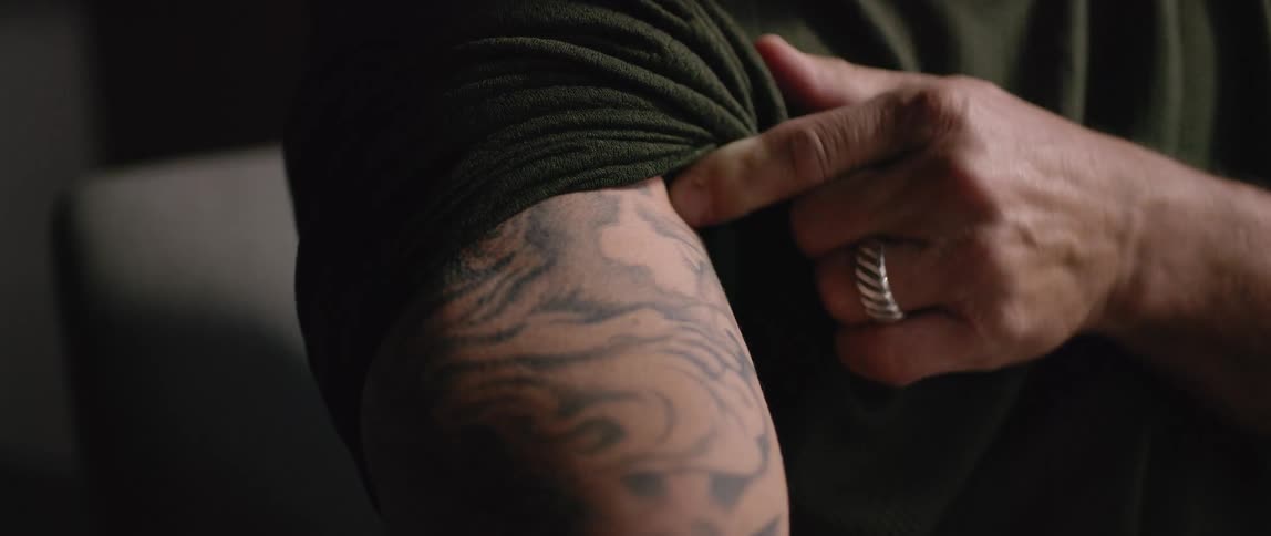 A man rolls up his sleeve revealing a tattoo on his right bicep
