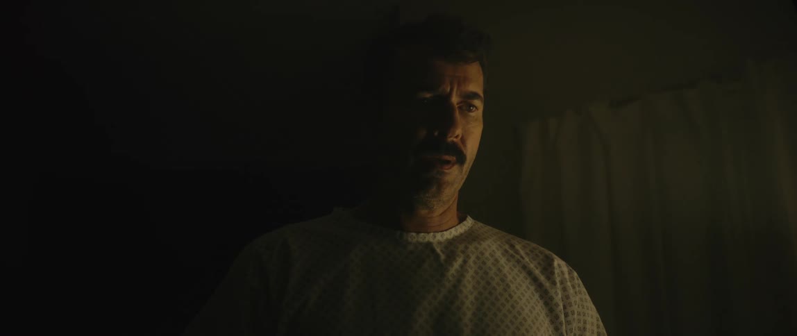 Male patient in hospital gown with scared face in dark room