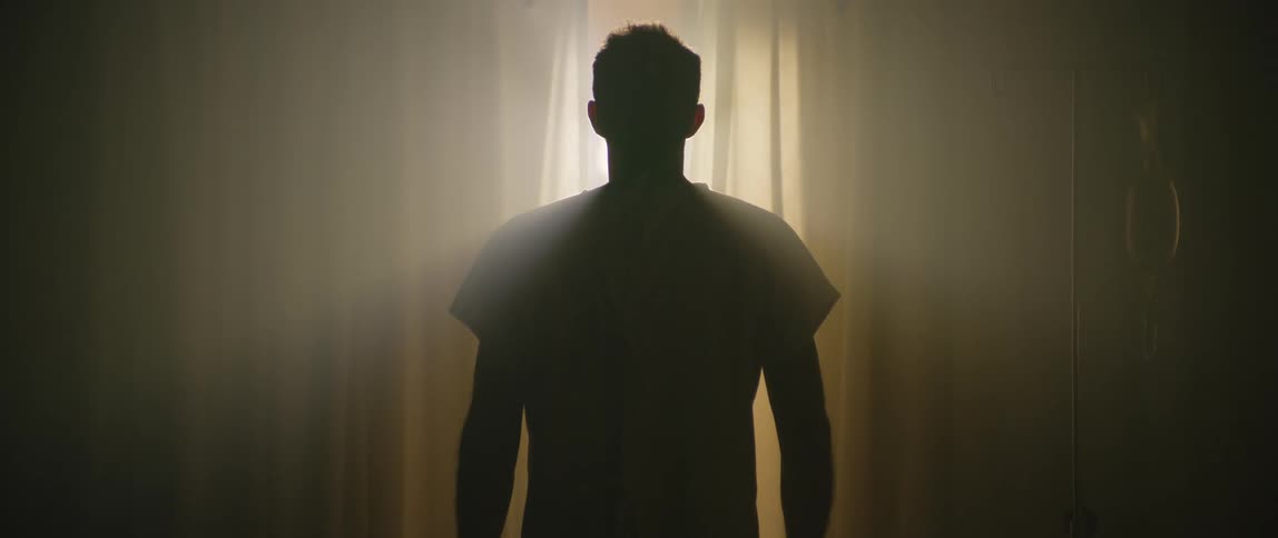 Back of a man standing in a dark hospital room at daytime