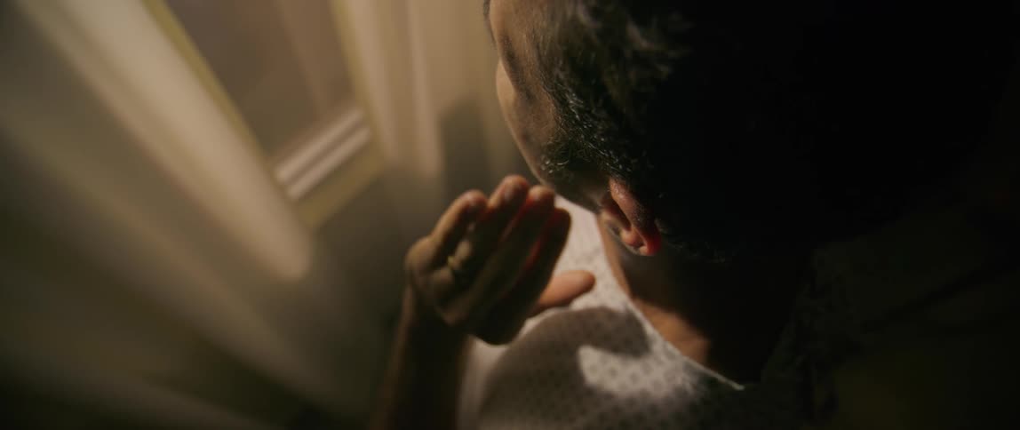 Overhead view of a patient placing his hand on his ear while facing a window in a room