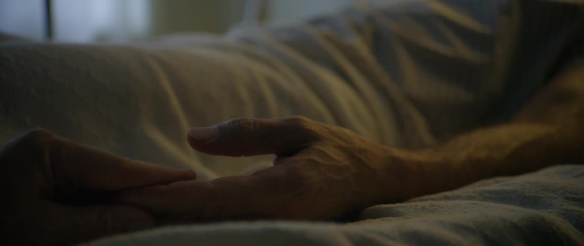 A tender moment is captured as two people gently hold hands while lying in bed conveying intimacy and care