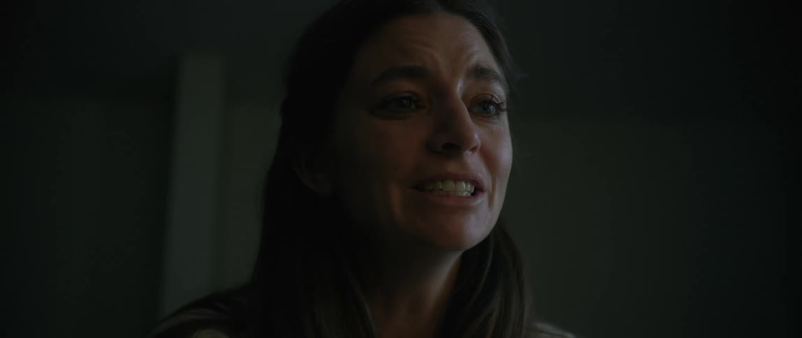 A distressed woman appears to be holding back tears in a dark tense interior setting possibly in a moment of emotional confrontation