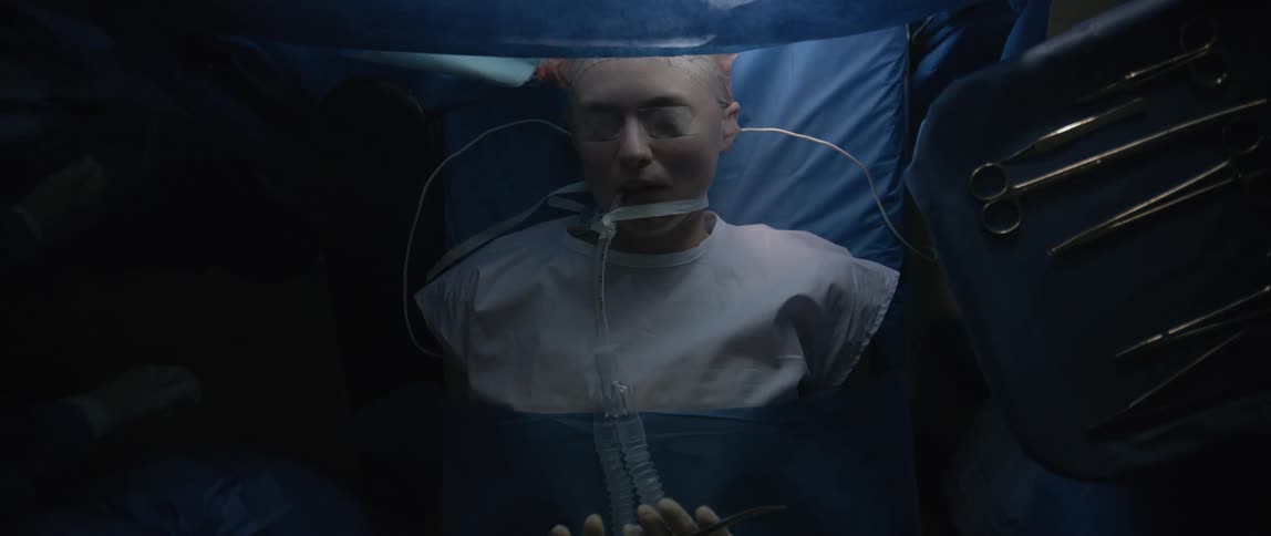 Group of surgeons surround an intubated patient and pass instruments around