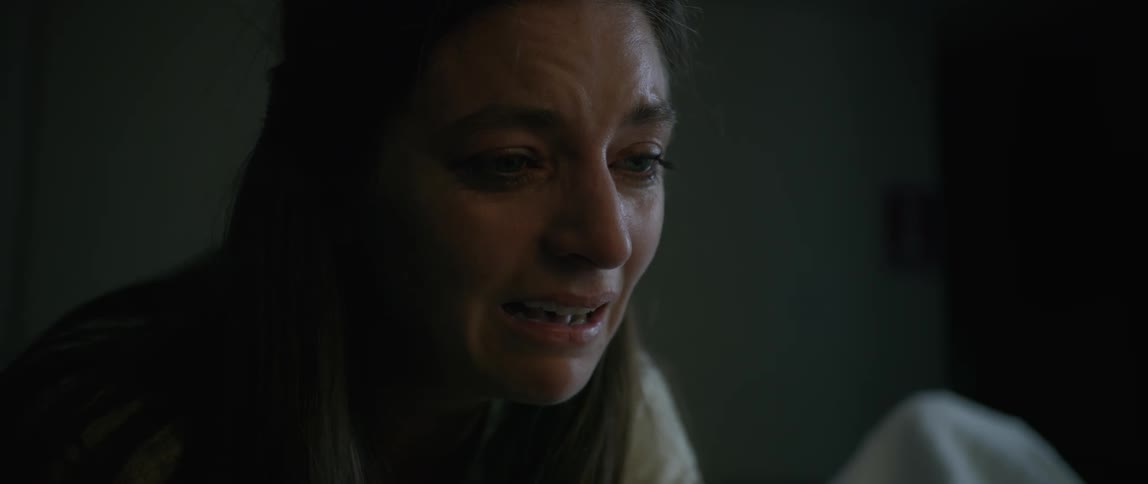 A woman cries and covers her mouth as she tries to speak