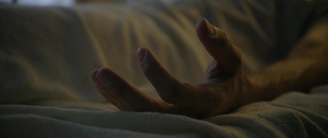 A sick patient clenches their hand in the hospital bed