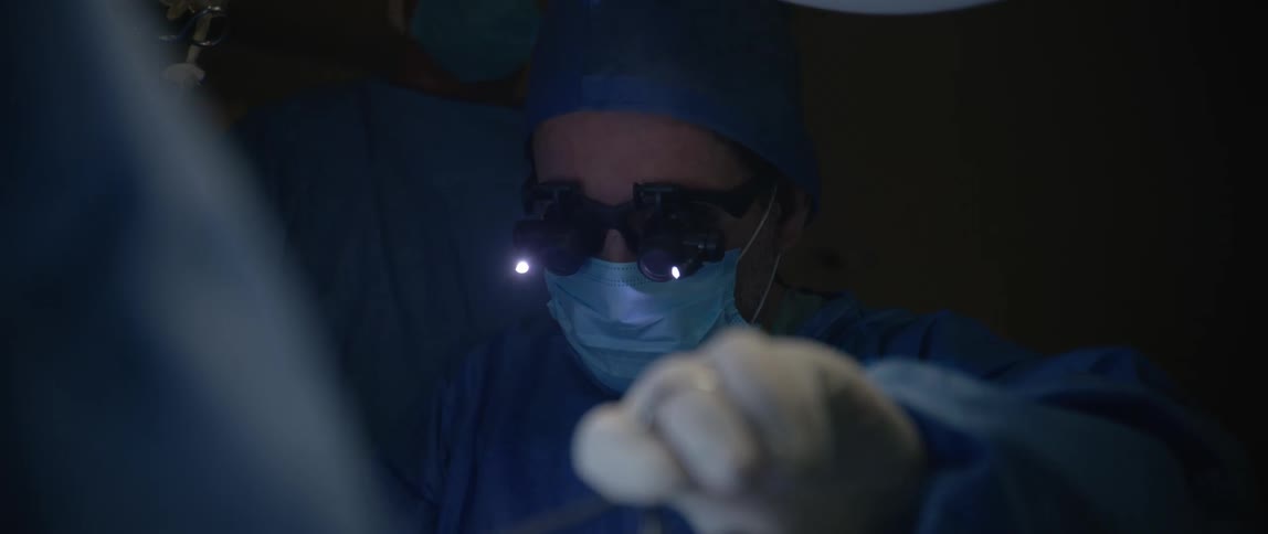 The doctor is operating on a patient while wearing surgical magnifying glasses