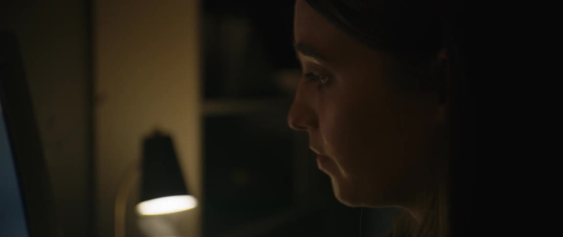 A woman is reading her computer monitor in the dark room