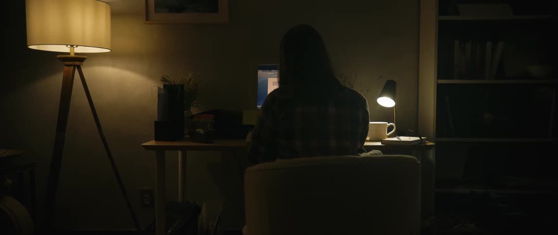 A solitary figure sits bathed in the warm glow of lamps working late into the night within a dimly lit room