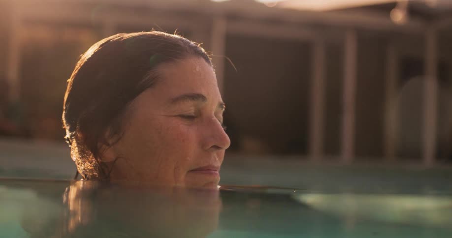 Profile of a woman standing neck high in swimming pool in her backyard