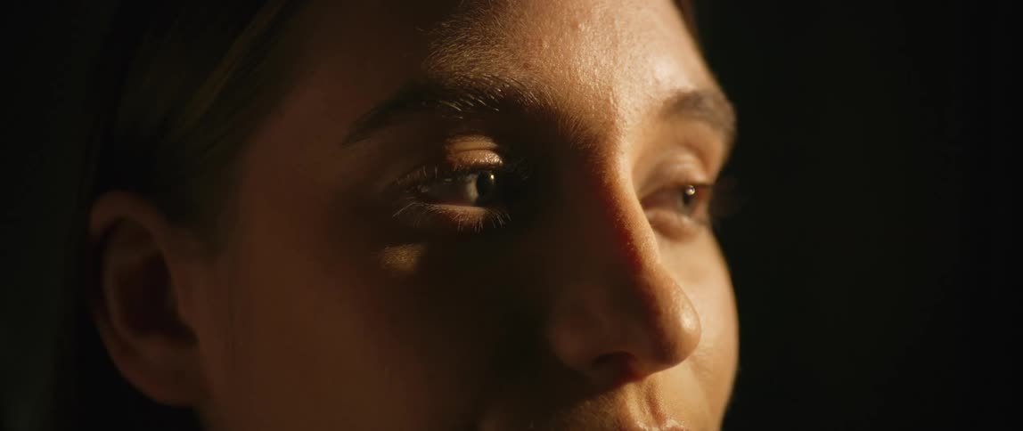 The face of a woman with fair skin that is partially illuminated and with her eyes closed and then she opens them