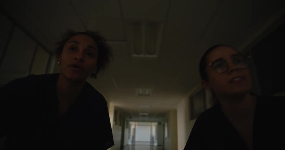 Two hospital workers are moving down the dark hallway