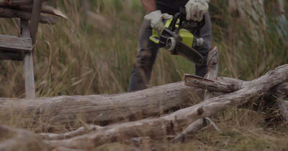 A man is using a chainsaw to cut a fallen tree