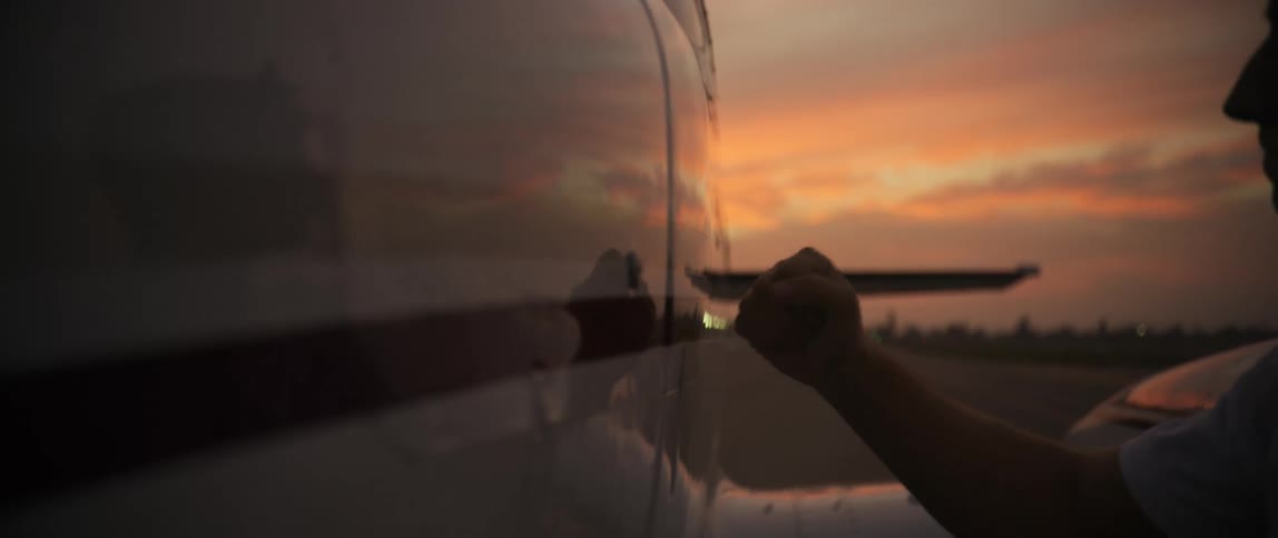 Man examines the exterior of a small plane parked on a runway under a red sky