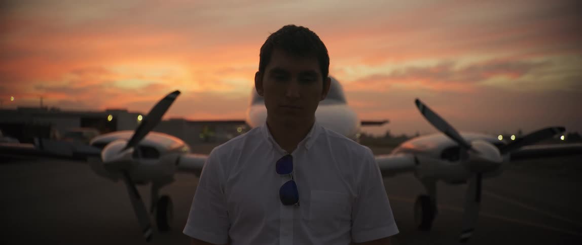 A pilot is standing on the runway in front of a plane