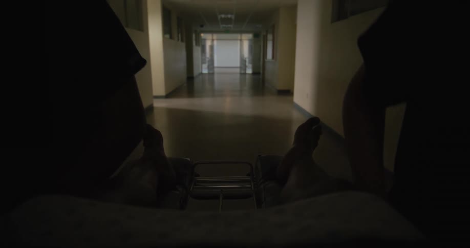 Patient in a hospital bed being rushed by medical professional through hospital corridor