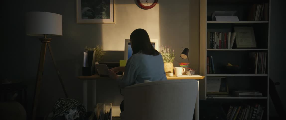 Woman consults a book while working on a computer on a desk at home