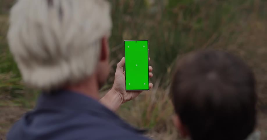 An older man and child look at the green screen on a phone