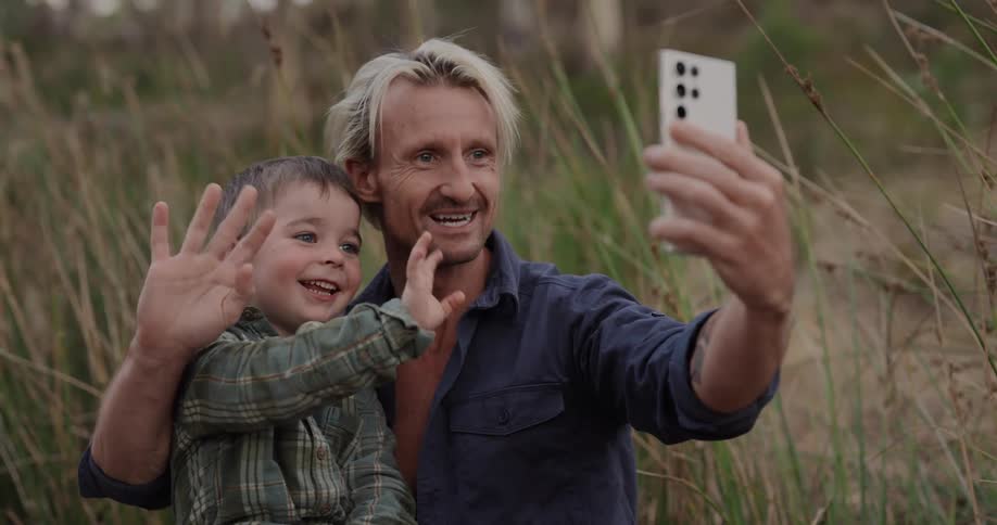 A father and son take a selfie in the grass