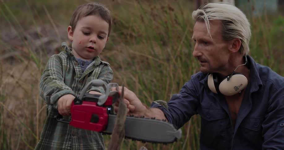 A father is showing his son how to use a toy chainsaw on a branch