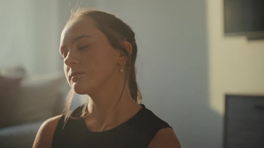 Woman keeps her eyes closed while stretching in her living room