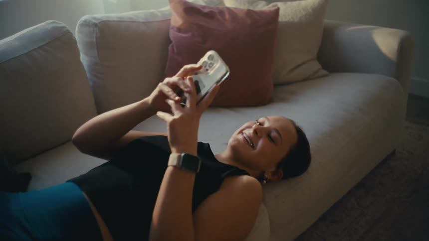 Happy woman lying on sofa and interacting with smartphone