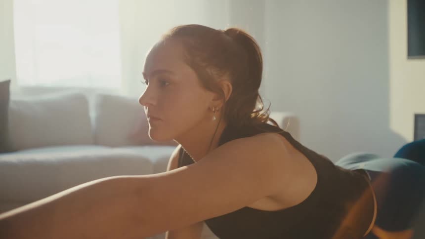 A young woman stretches on the floor in a sunlit living room engaged in a home workout