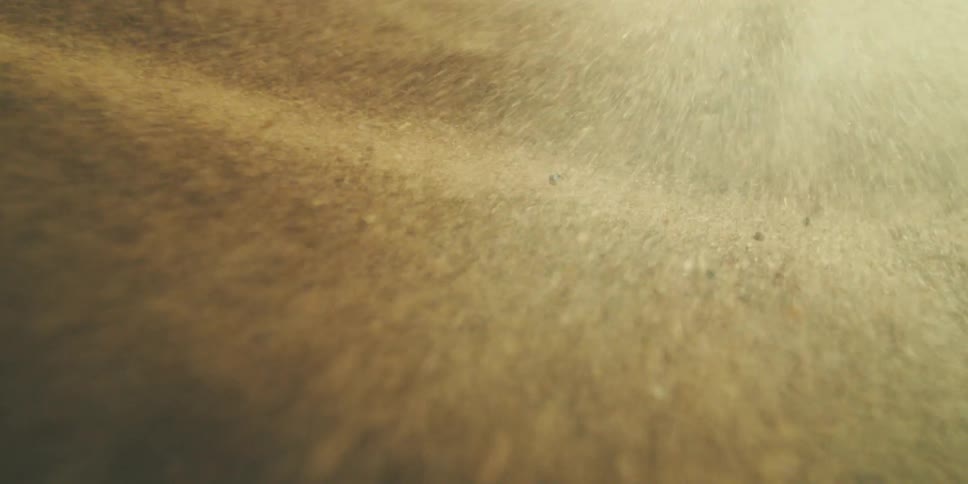 A dramatic closeup captures fine particles or sand swirling in slow motion creating a surreal textured landscape