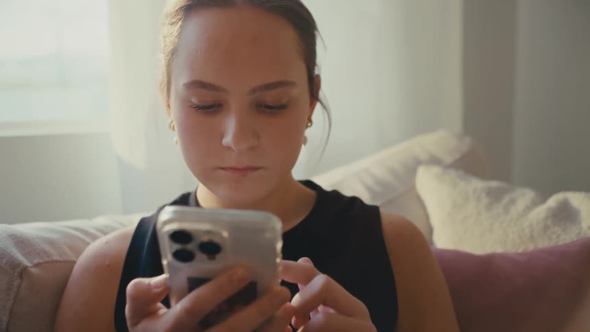 A young woman is engrossed in her smartphone while relaxing on a couch