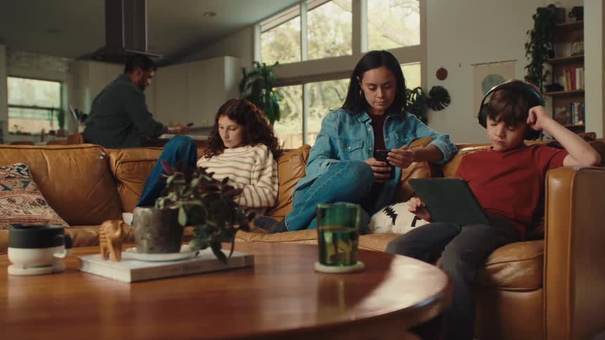 A family is relaxing together at home each engrossed in their own digital device or activity