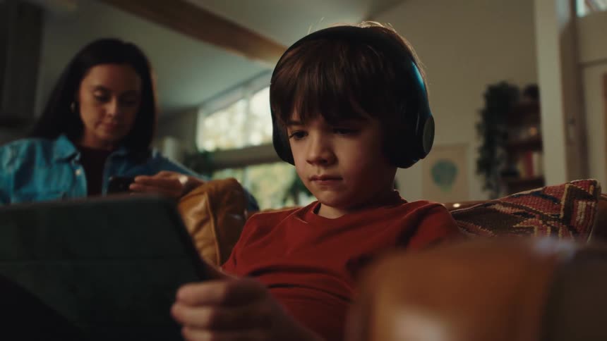 A footage of a boy sitting beside his mother and operating a tablet