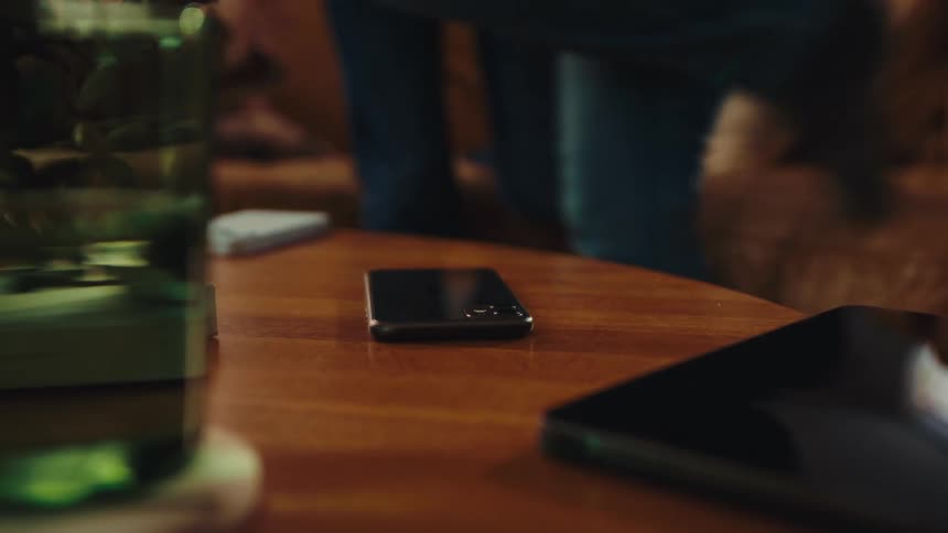 Three people placing their cell phones on coffee table then getting off the couch
