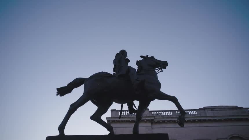 A statue of a man on a horse on a pedestal near a palace