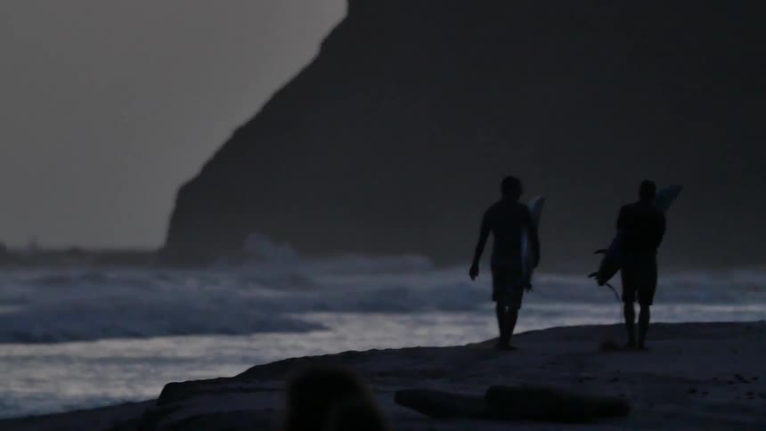 People walk along the shore carrying surfboards at dawn