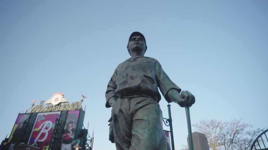A statue holding a stick stands in the middle of the street at midday