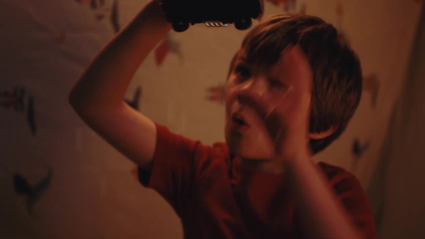 A boy wearing a brown tshirt is playing with a toy car