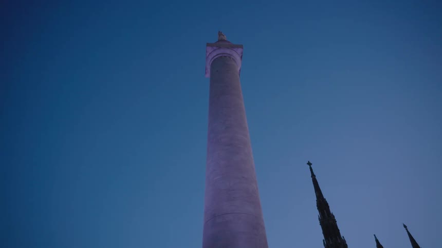 A large round concrete pillar with a sculpture on top against a blue sky