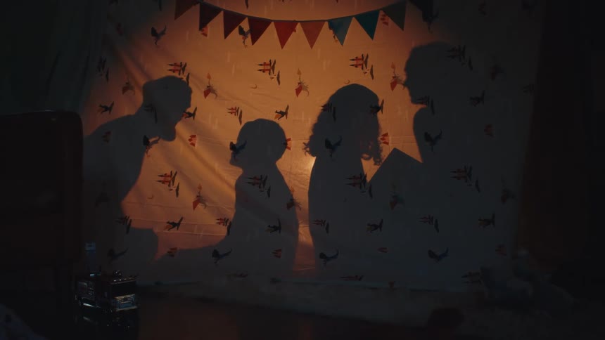 Silhouettes of a group of people who are playful and having a conversation behind a cloth barrier at night