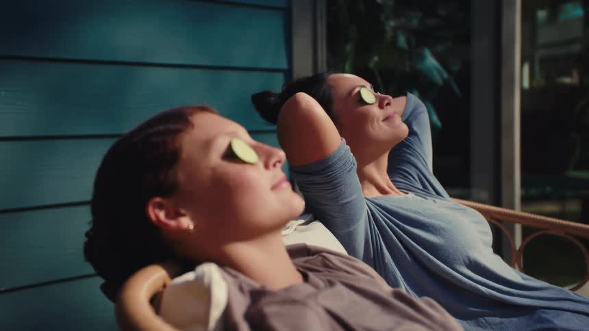 Two women rest under the sun with cucumber slices on their eyes