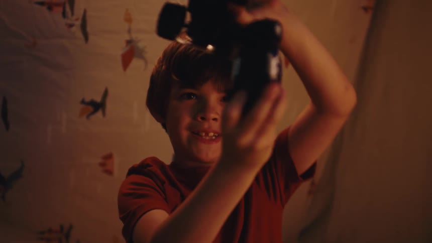A boy is playing with a toy car and toy monster truck smashing them together