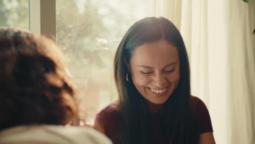 Two women laugh while conversing as one paints the nails of the other person