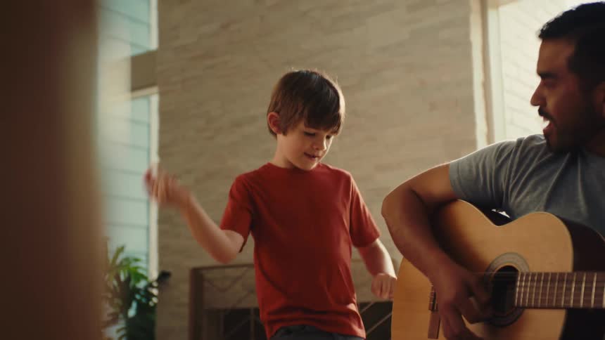 Young boy dancing as his dad is singing and strumming on an acoustic guitar