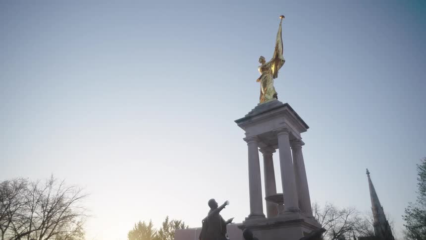 The sun is rising by the monument with statues of people