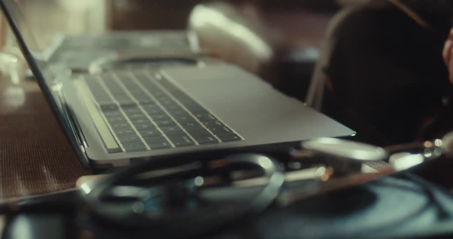A stethoscope rests on a black medical bag beside an open laptop on a desk in a softly lit room